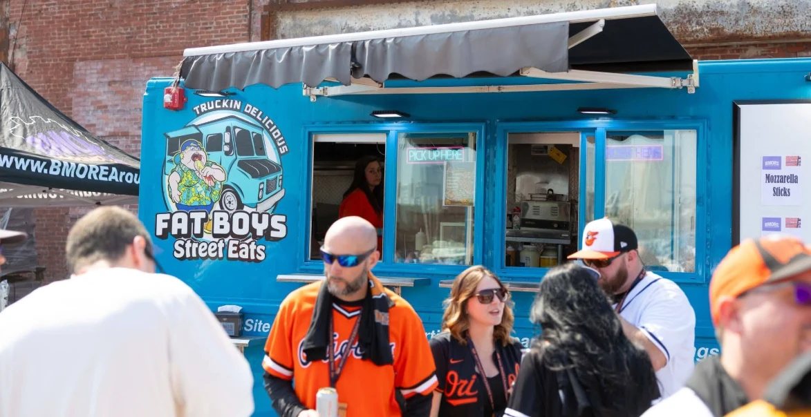 Customers gathered at the Fat Boys Street Eats truck at a Baltimore street event, awning out and the pick-up window open